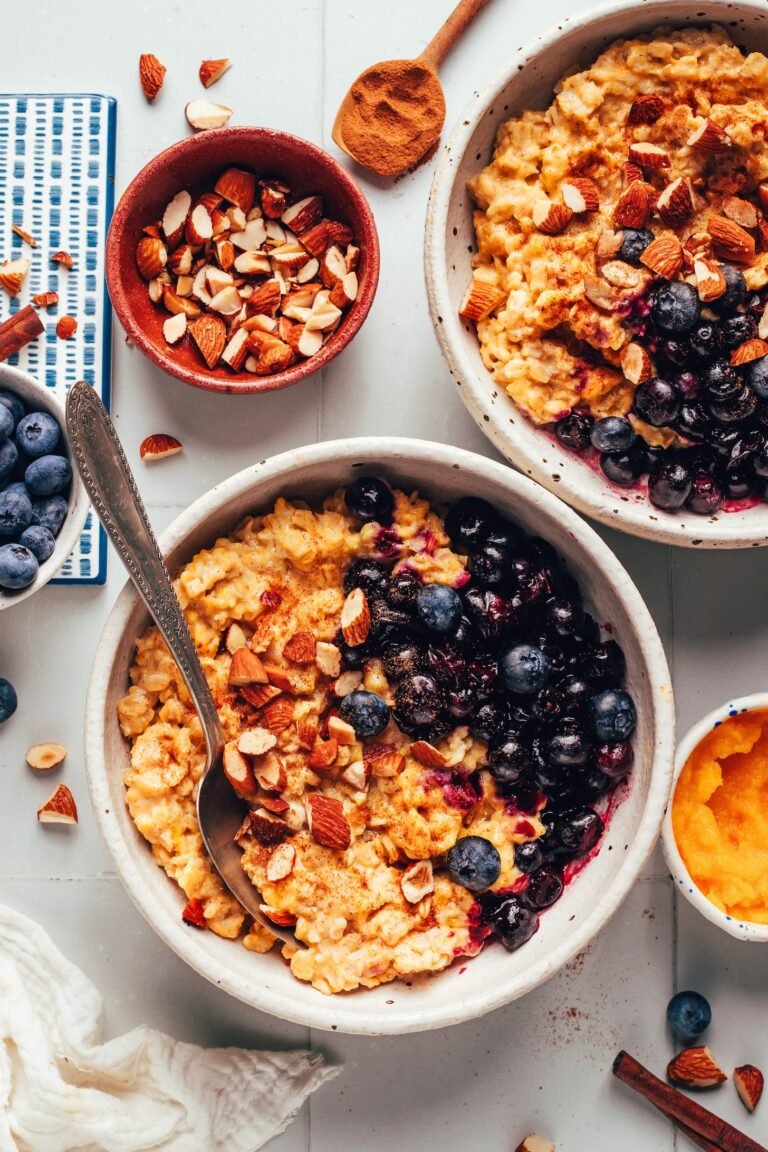 Two bowls of creamy pumpkin oats topped with blueberries and toasted almonds