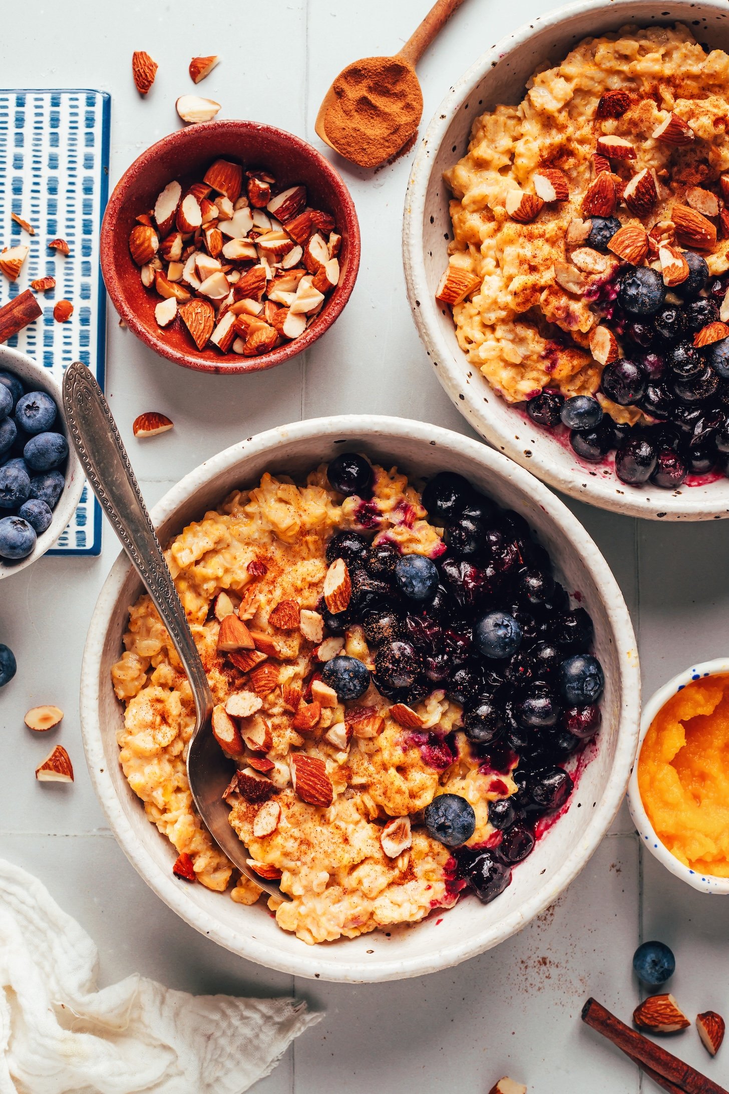 Two bowls of creamy pumpkin oats topped with blueberries and toasted almonds