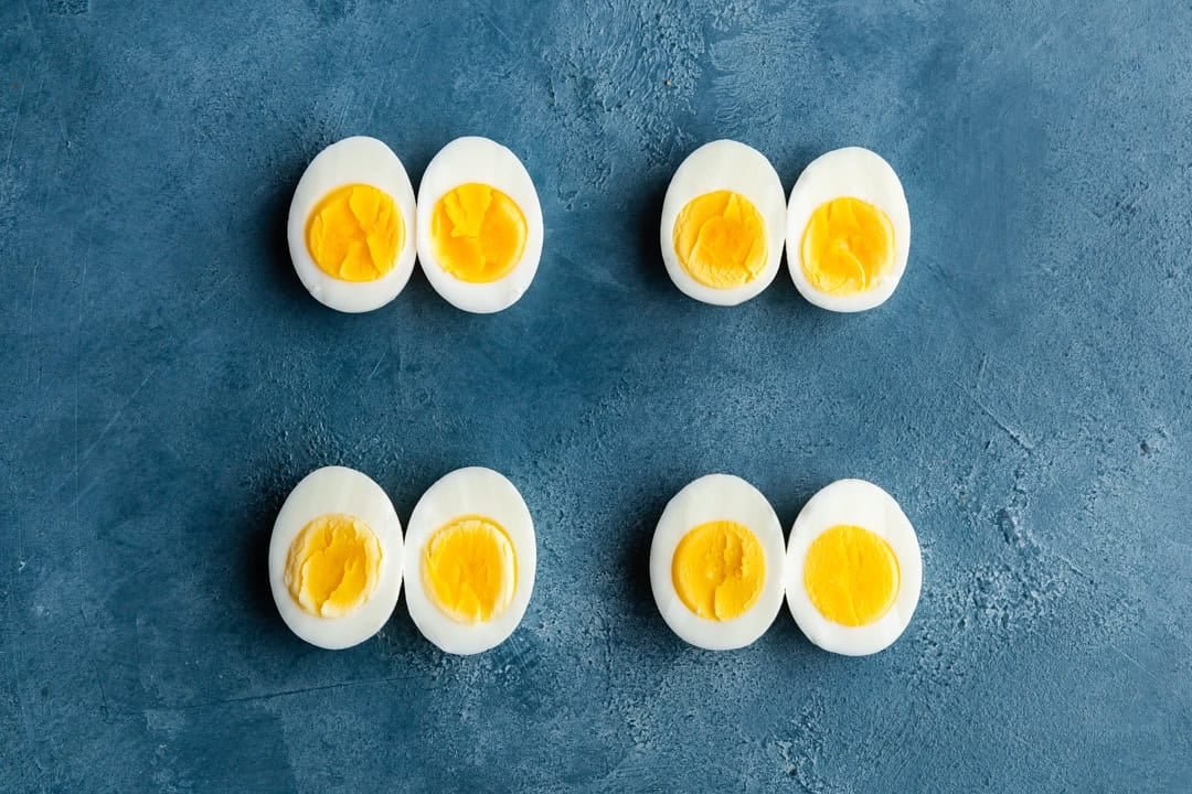 Overhead shot of 4 cut in half versions of eggs boiled at different times.