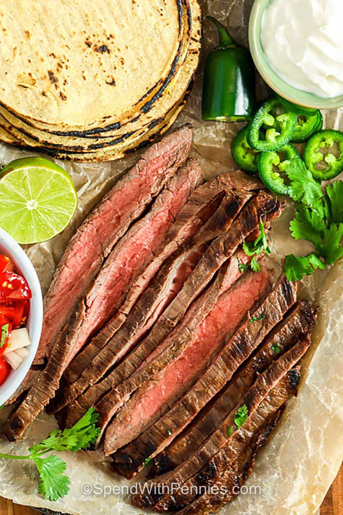 plate of sliced Carne Asada with vegetables and torilla and sour cream
