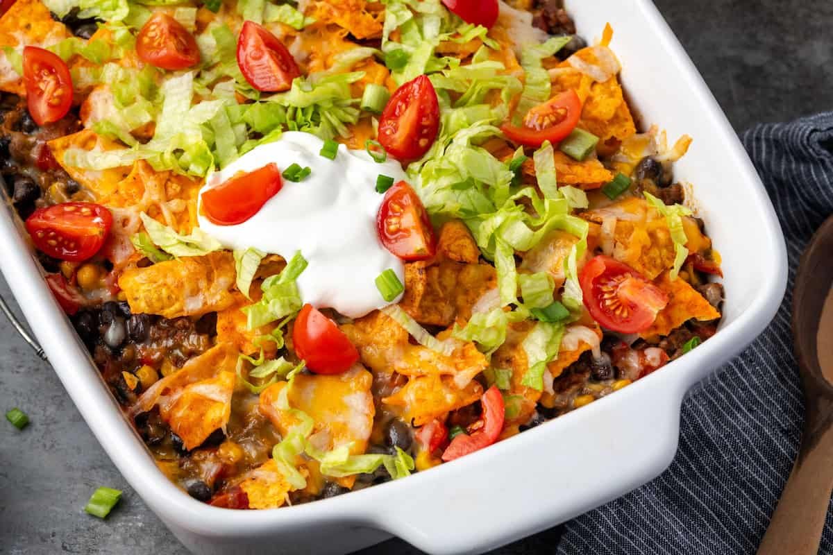 Taco casserole topped with a dollop of sour cream in a ceramic baking dish.