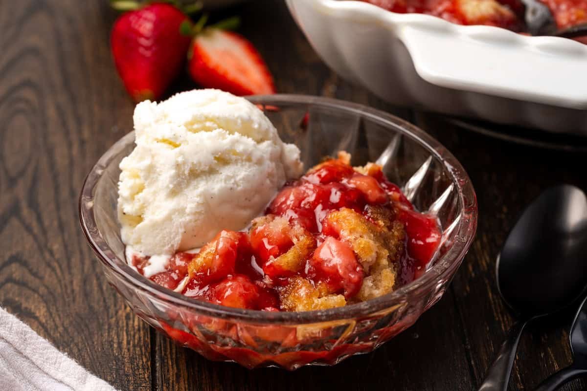 A serving of strawberry cobbler in a bowl topped with vanilla ice cream.