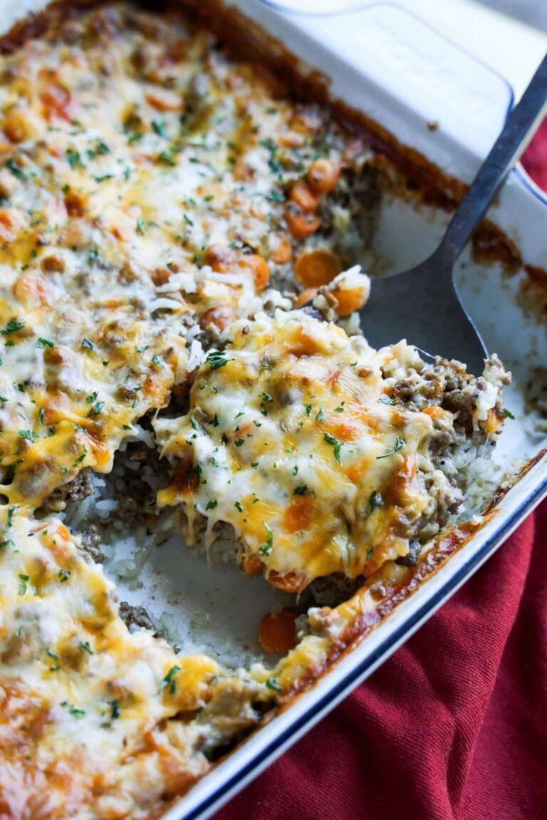 Cheese topped rice and ground beef casserole baked in a white ceramc baking dish with a spoon serving a piece